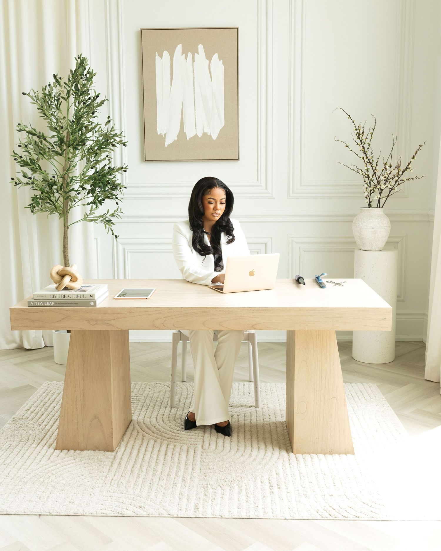 Woman working on laptop at a light wood desk in a bright, minimalist home office with abstract wall art.