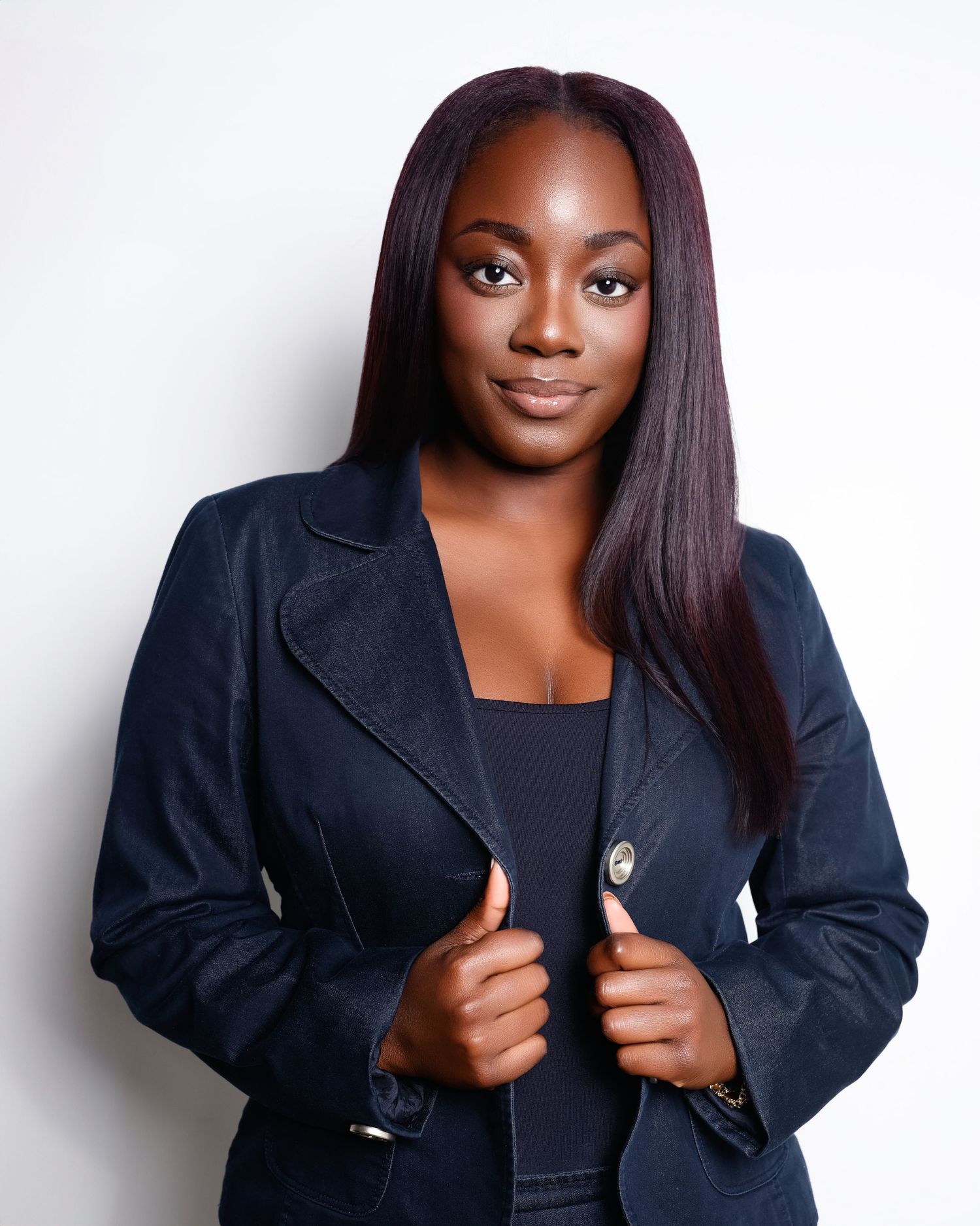 Young woman in black in blazer poses confidently against a white background.