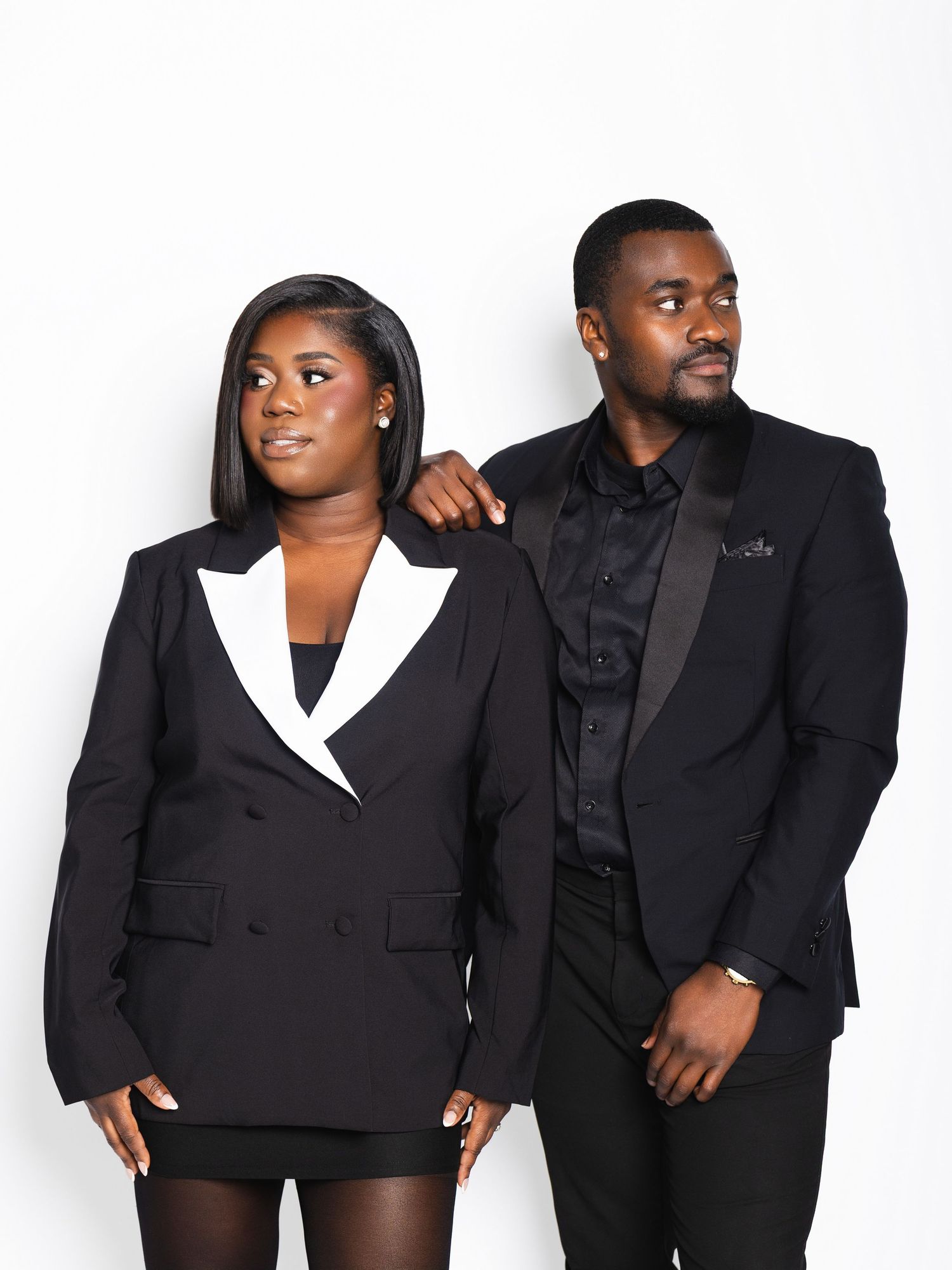 A woman and man in matching black blazers posing together against a clean white background.