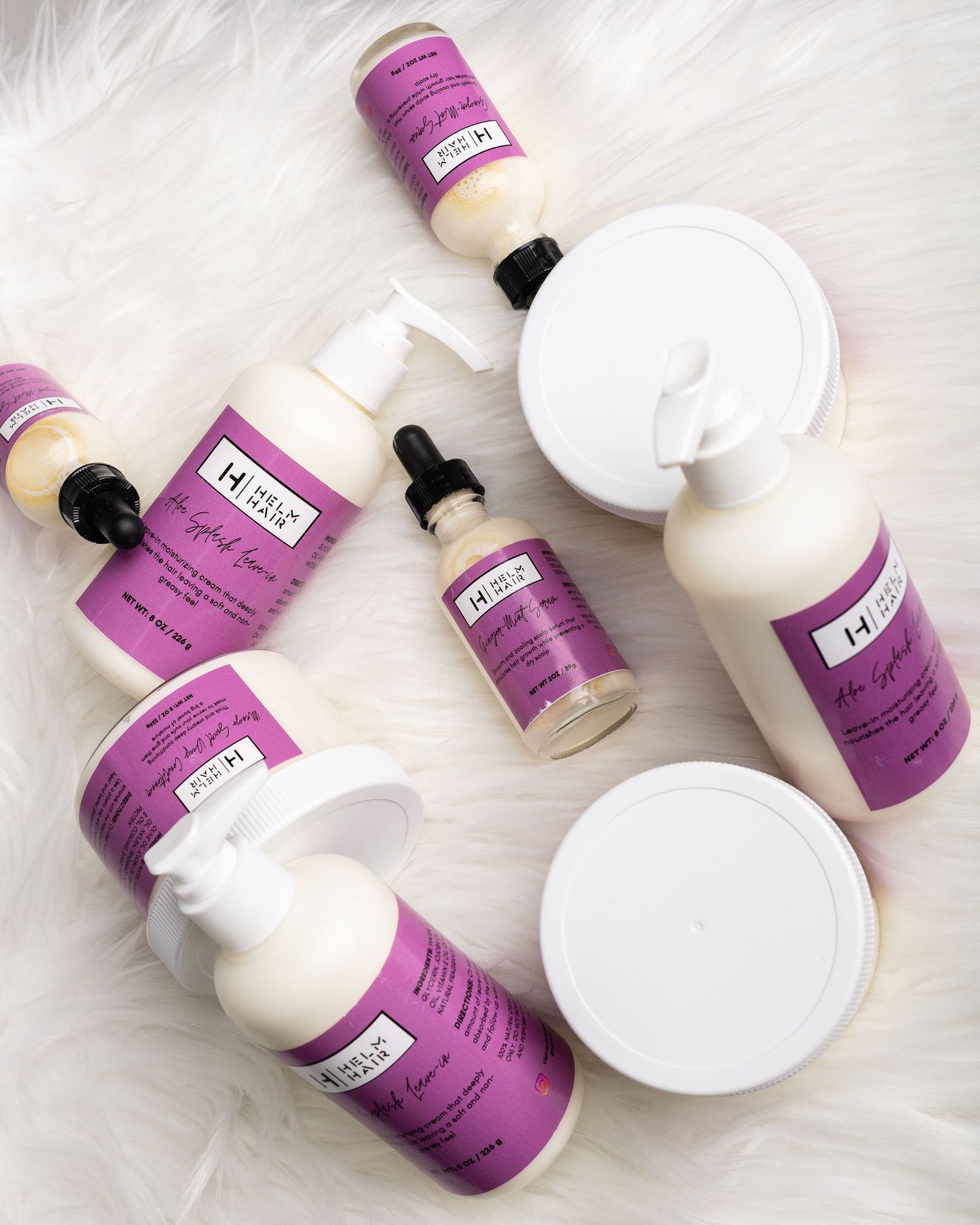 Flat lay of purple-labeled H haircare product collection including bottles, pumps, and jars on white background.
