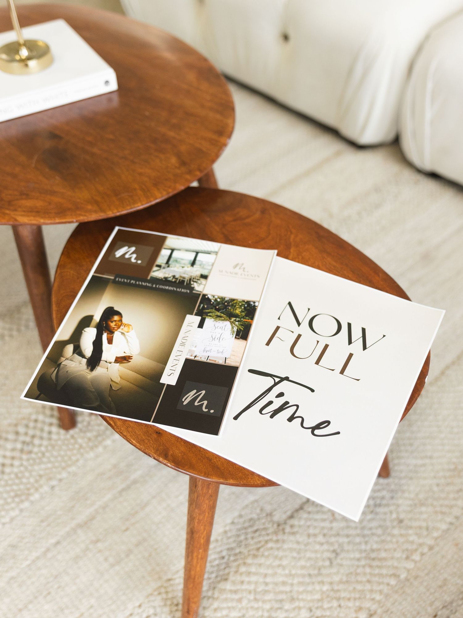 Wooden nesting tables displaying photography prints and a “Now Full Time” sign, styled on a cozy living room rug.