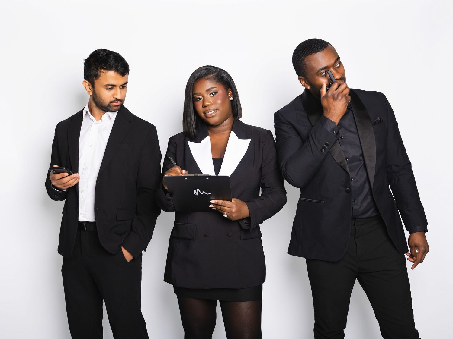 Three business professionals in black suits posing together, two men flanking a woman against white backdrop.