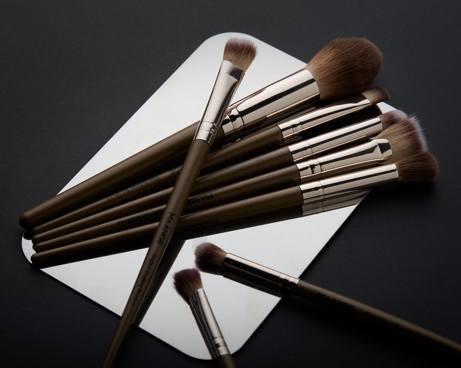Set of professional makeup brushes with wooden handles arranged on a white palette against a dark background.