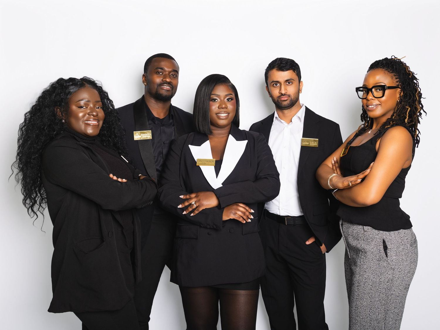Five diverse colleagues in black business wear posing confidently against white background.