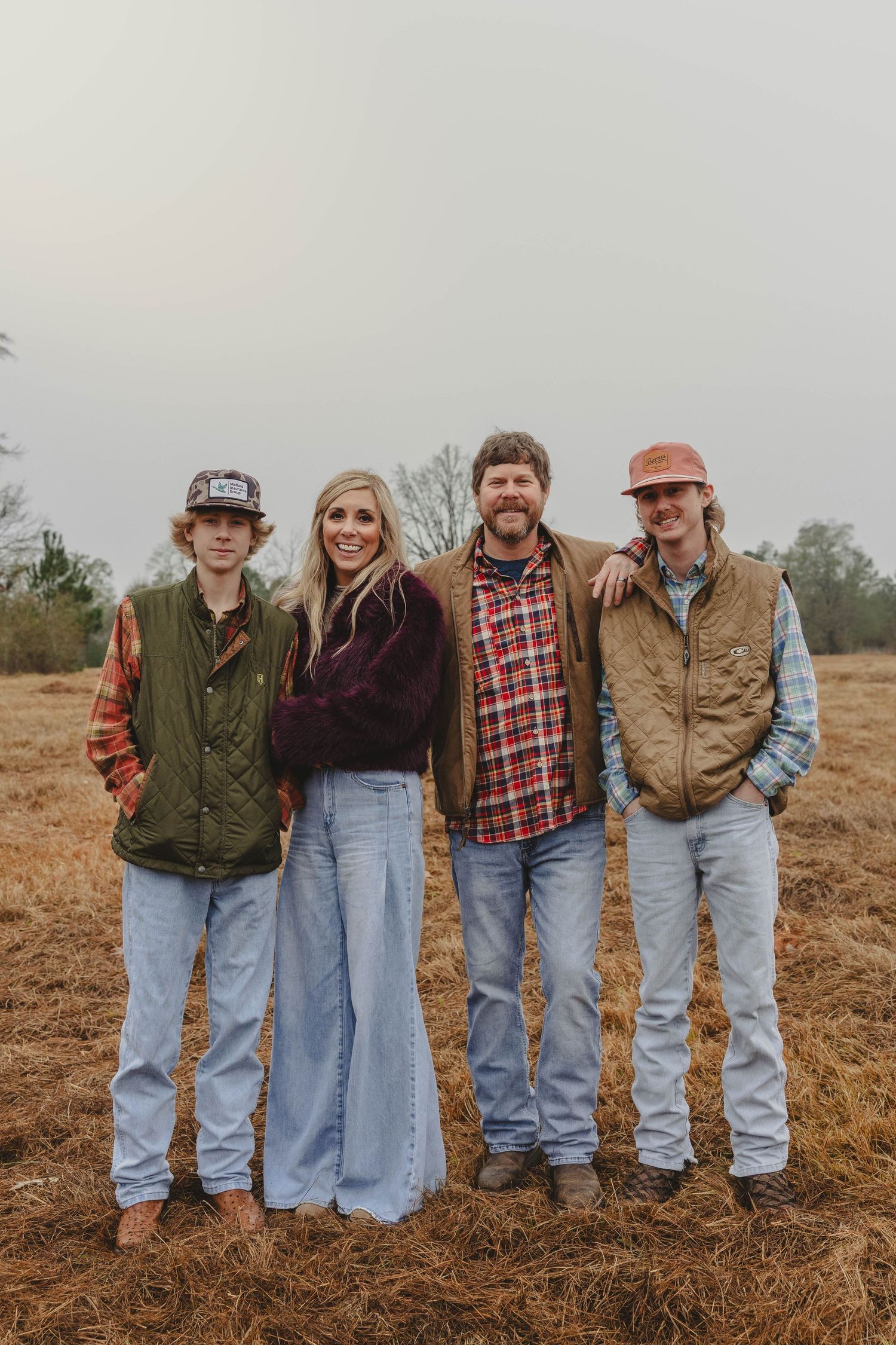 A group of people stand together in casual clothing on a plowed field during an overcast day.
