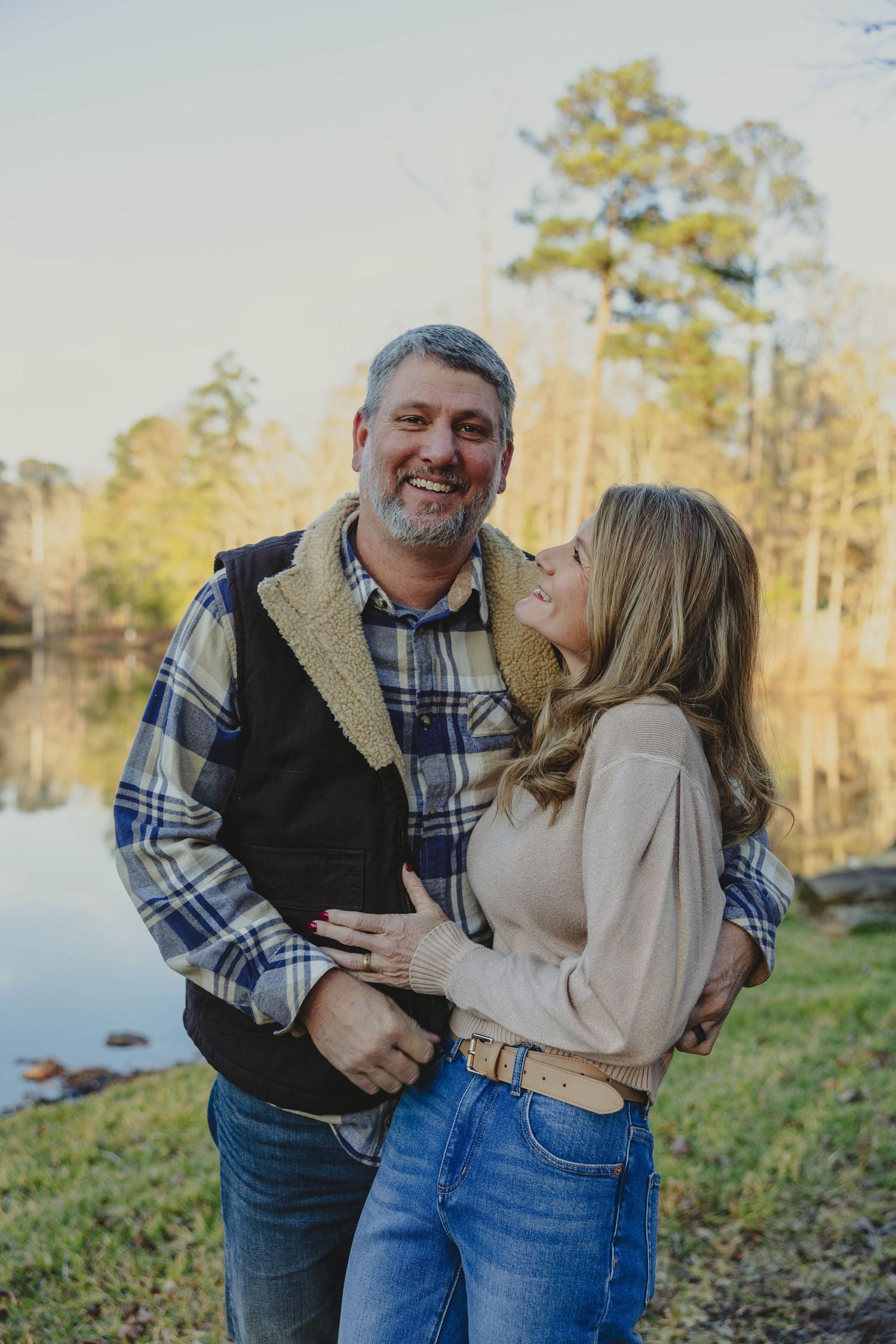 A couple shares a joyful moment together outdoors near a lake on an autumn afternoon.