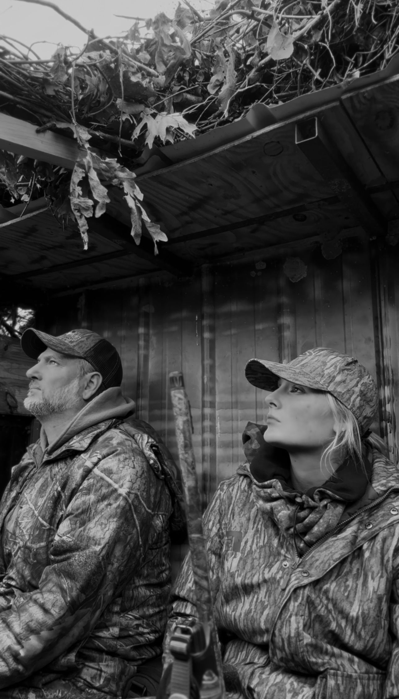 Black and white photo of hunters waiting in a camouflaged duck blind.