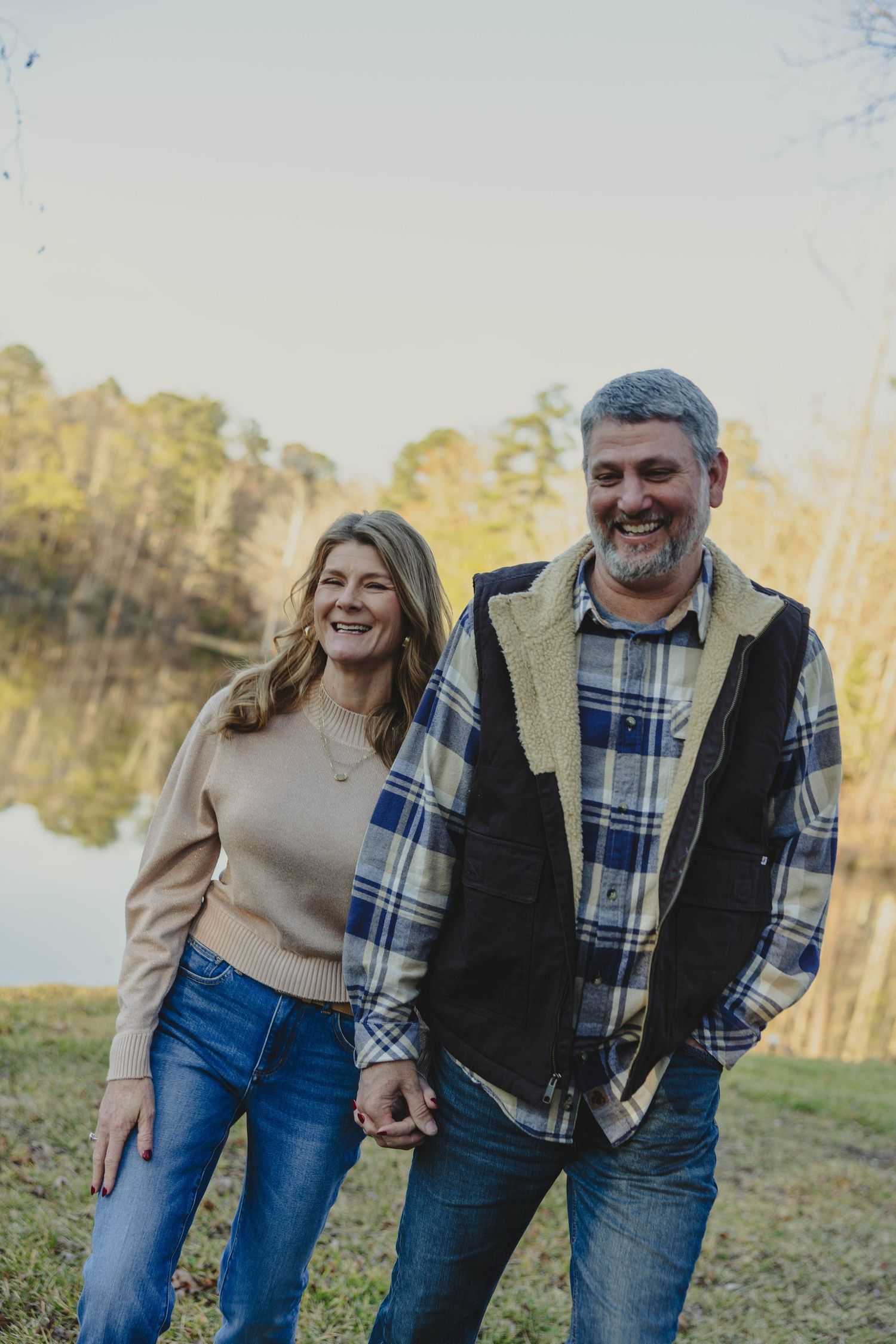 A couple laughs together while walking along a lakeside path during golden hour.