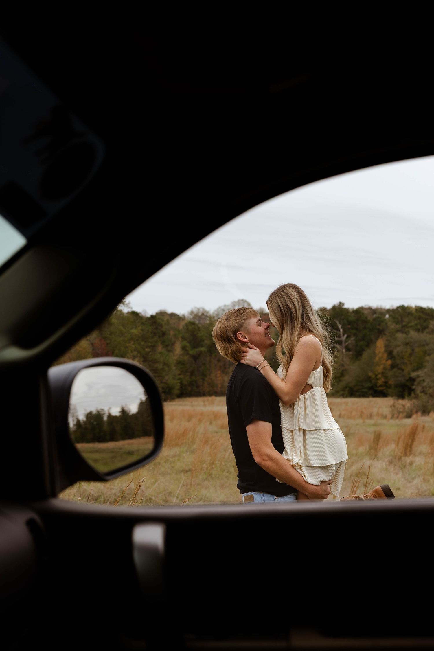 Romantic moment captured through a car window in a rural field setting.