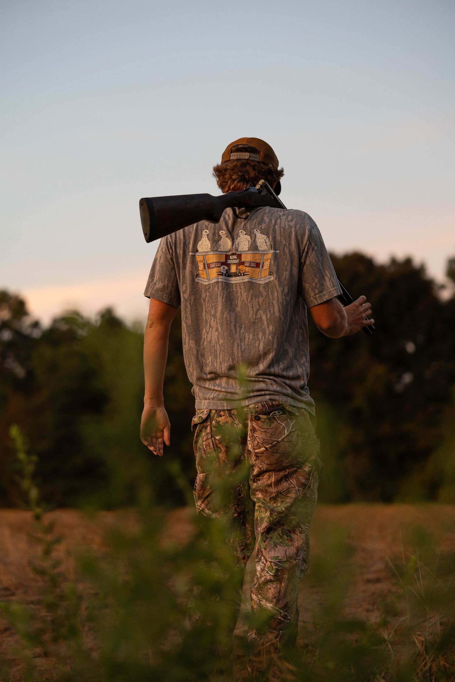 Hunter walking through field at sunset in camouflage gear.