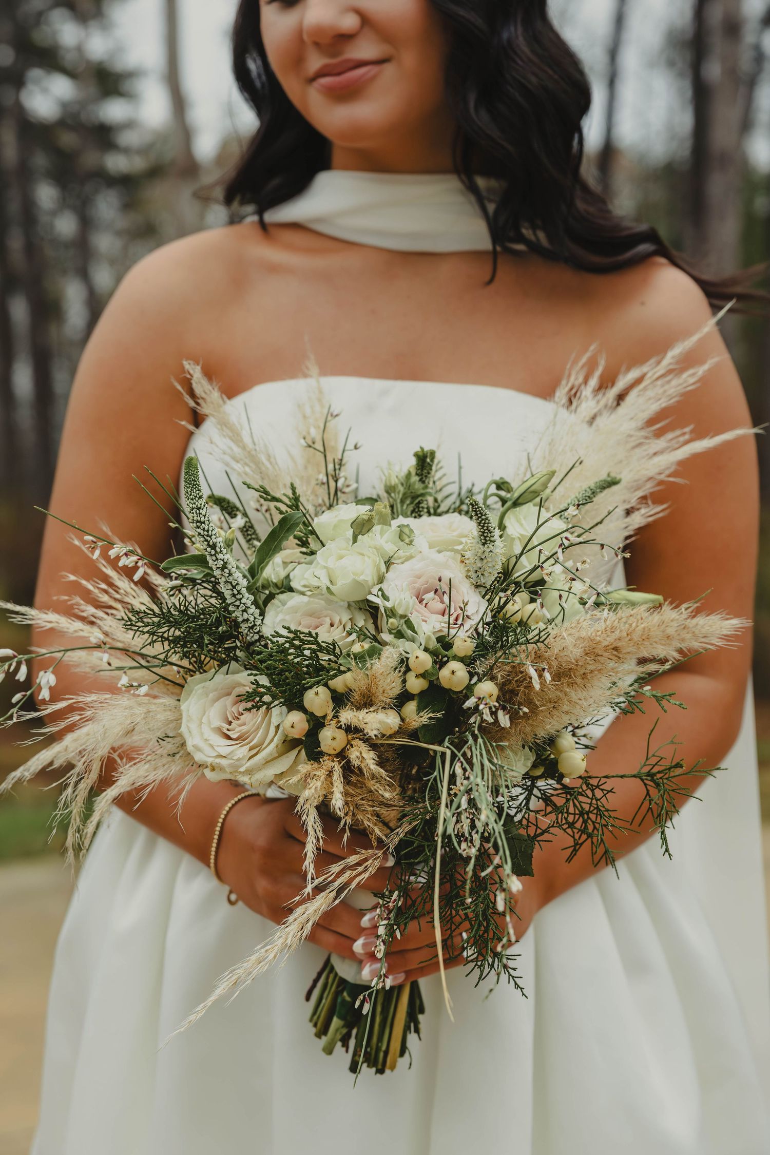 A series of elegant white and green wedding bouquets with dried pampas grass and delicate florals held against white dresses.