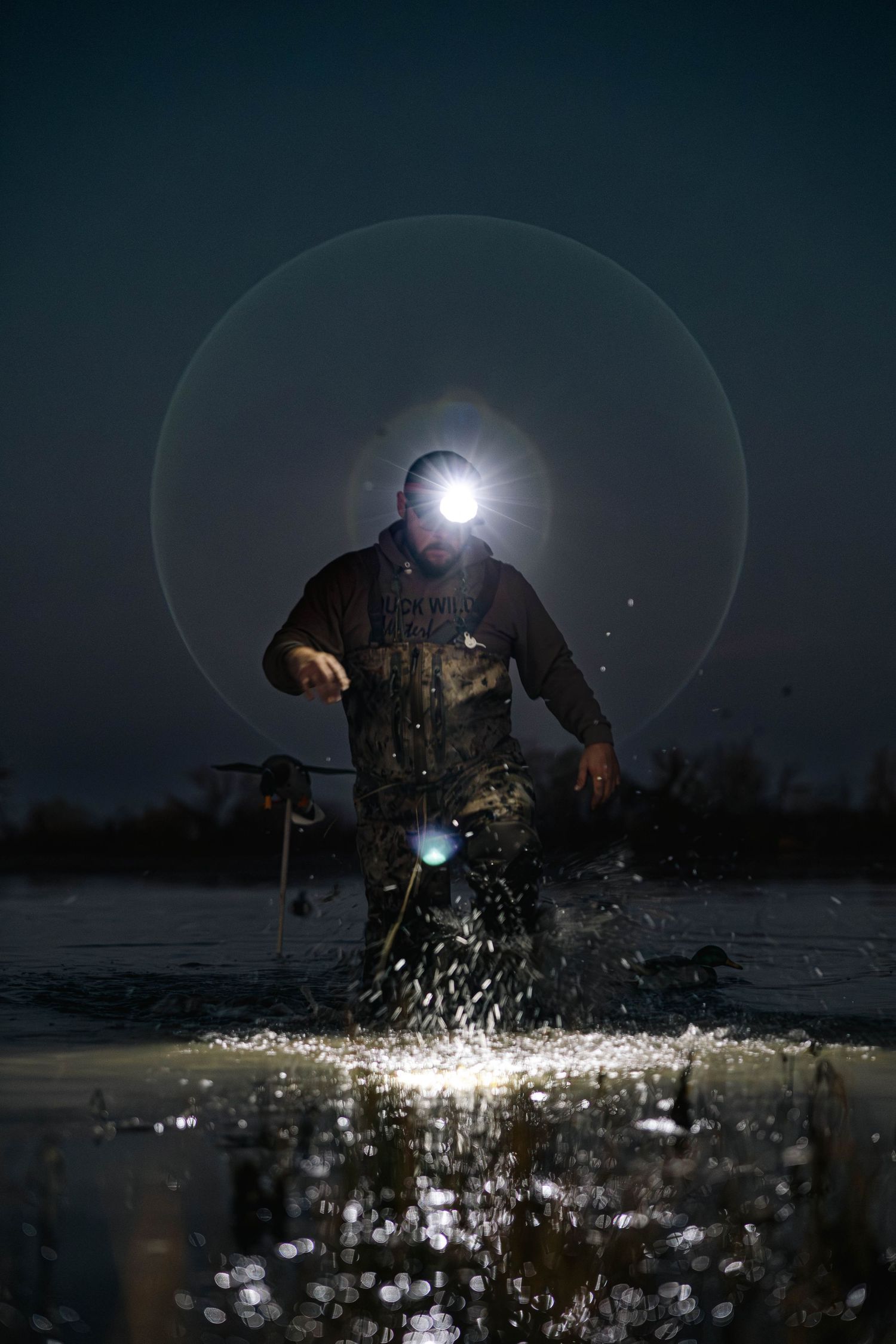 Ice fisherman with headlamp breaks through frozen surface at night creating dramatic splash effect.
