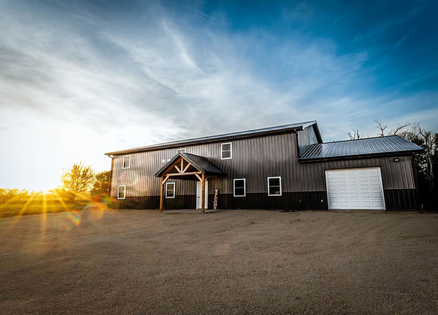 A panoramic view of a rural barn building against a dramatic blue sky with sunburst at sunset.