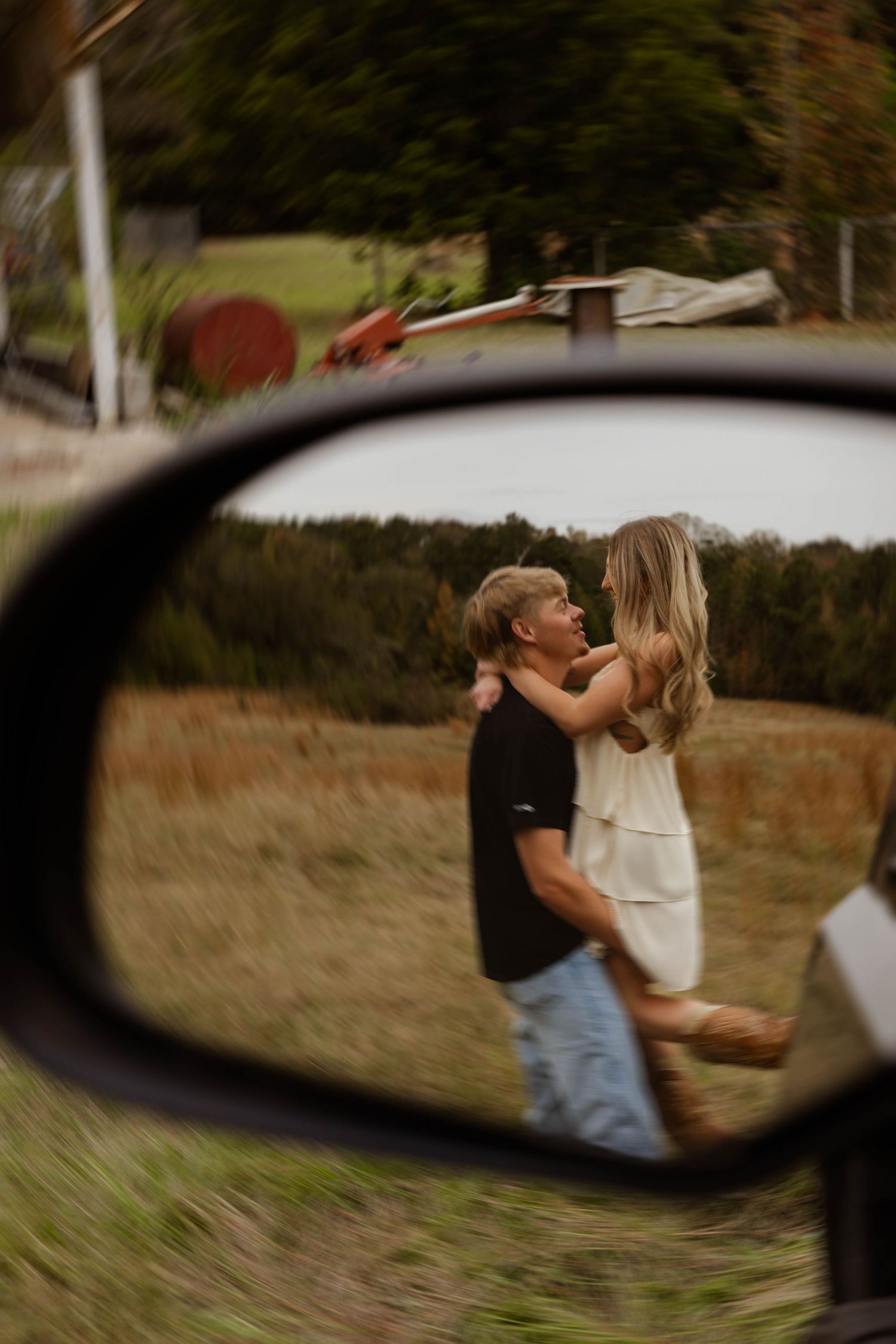 Romantic couple reflected in car side mirror during sunset.