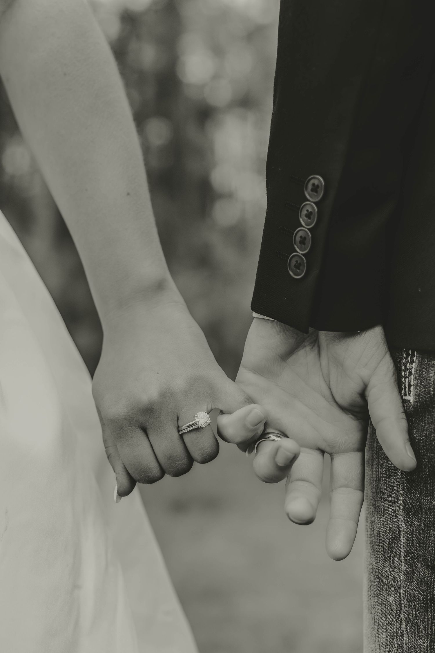 Black and white close-up image of two people holding hands against a blurred background.