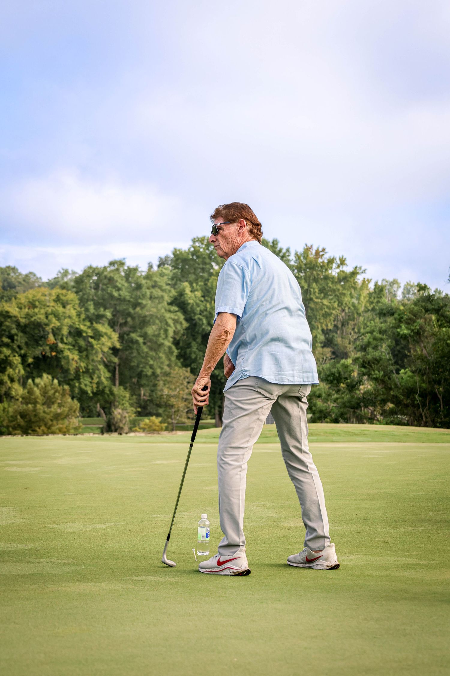 Golfer on putting green lining up shot on sunny day.