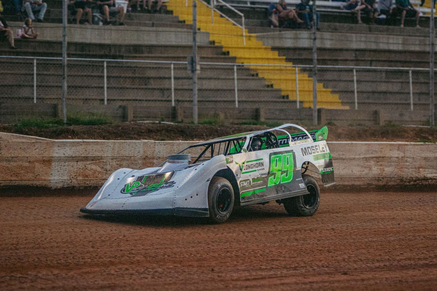 Green and white dirt track race car kicking up dust on oval racing circuit.