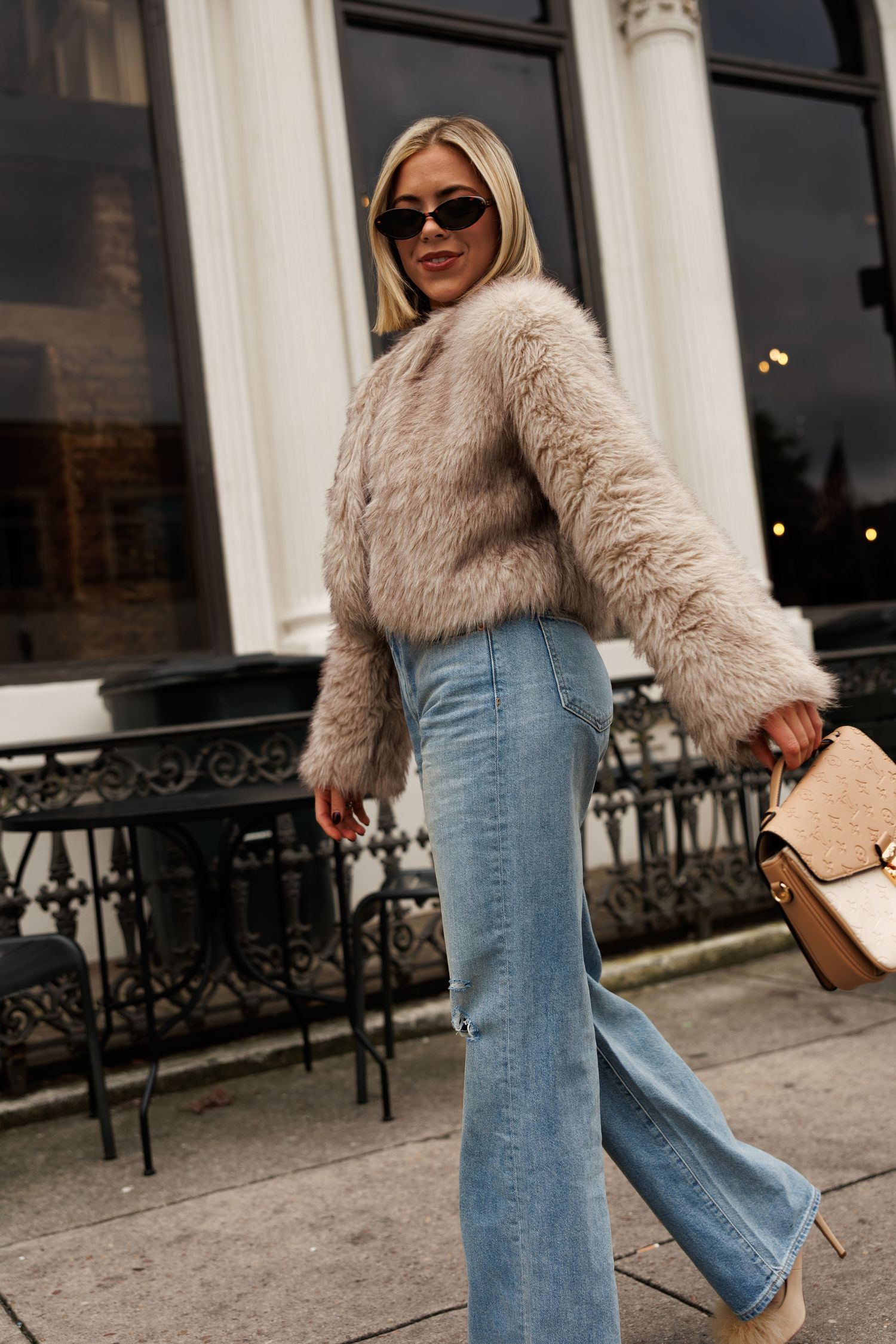 Stylish winter outfit featuring a beige fur coat paired with light wash wide-leg jeans and accessorized with sunglasses.