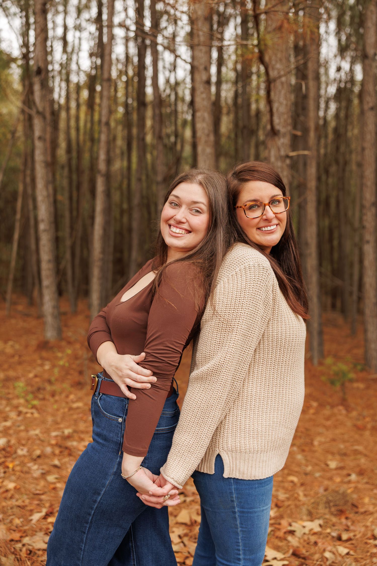 Two friends share joyful hugs and laughter in a scenic autumn forest with fallen leaves.