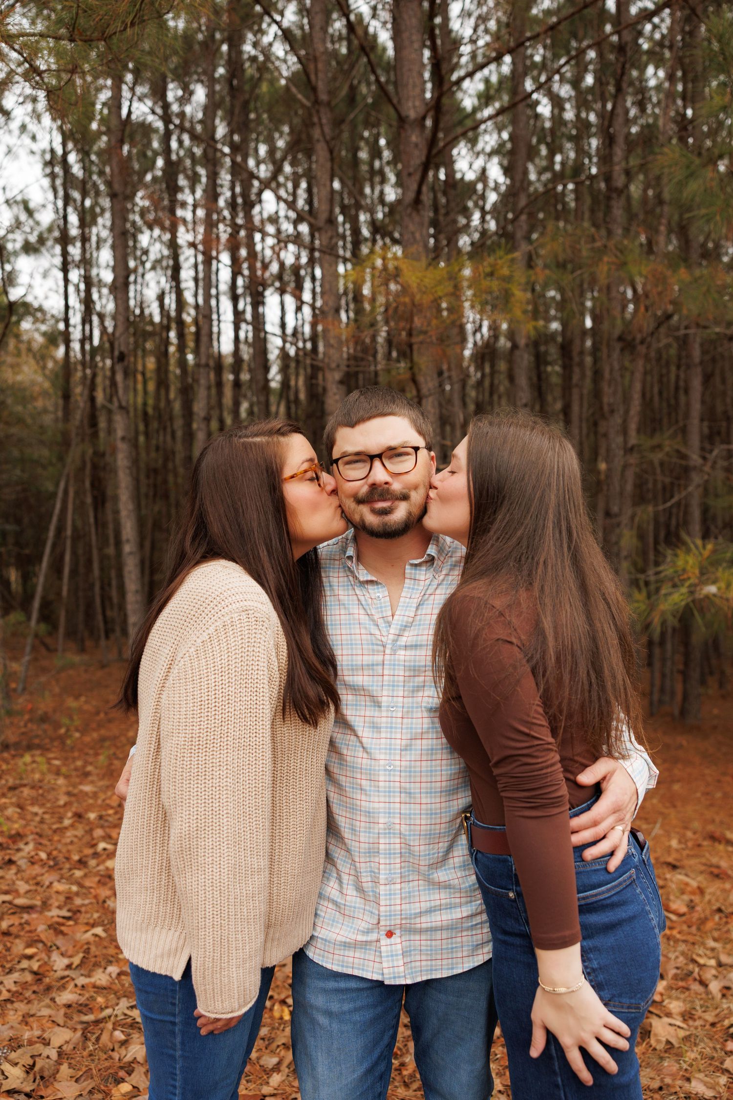 Three people pose together on fallen autumn leaves in a wooded forest setting.