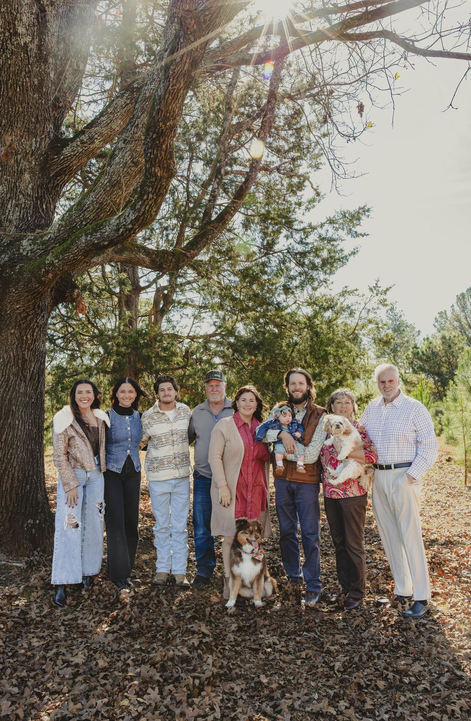A group of people standing together outdoors against a backdrop of trees on an autumn day.