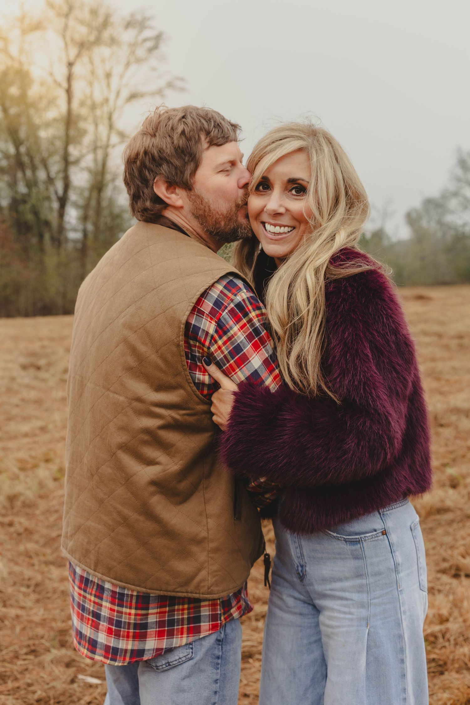 A couple shares tender moments in a field wearing casual fall attire and embracing on an autumn day.