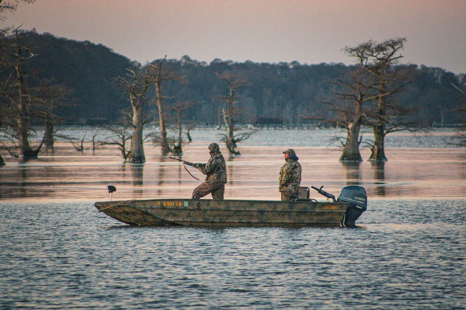 Hunters in camouflage gear setting up decoys in a flooded marsh at sunrise.