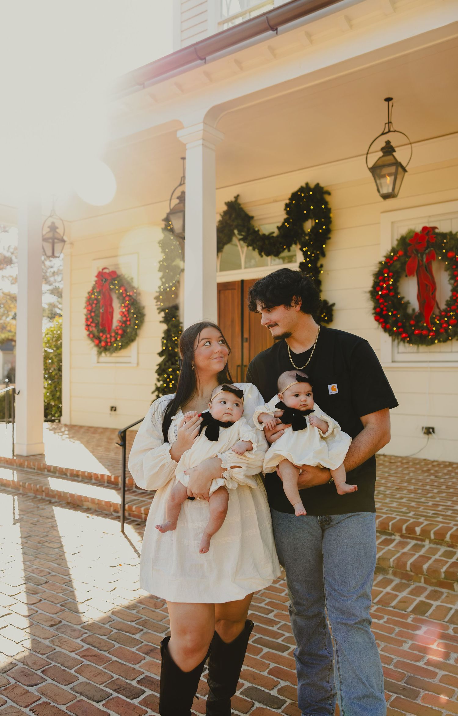 A sequence of five candid outdoor photos showing a couple holding a baby on a porch decorated with Christmas wreaths.