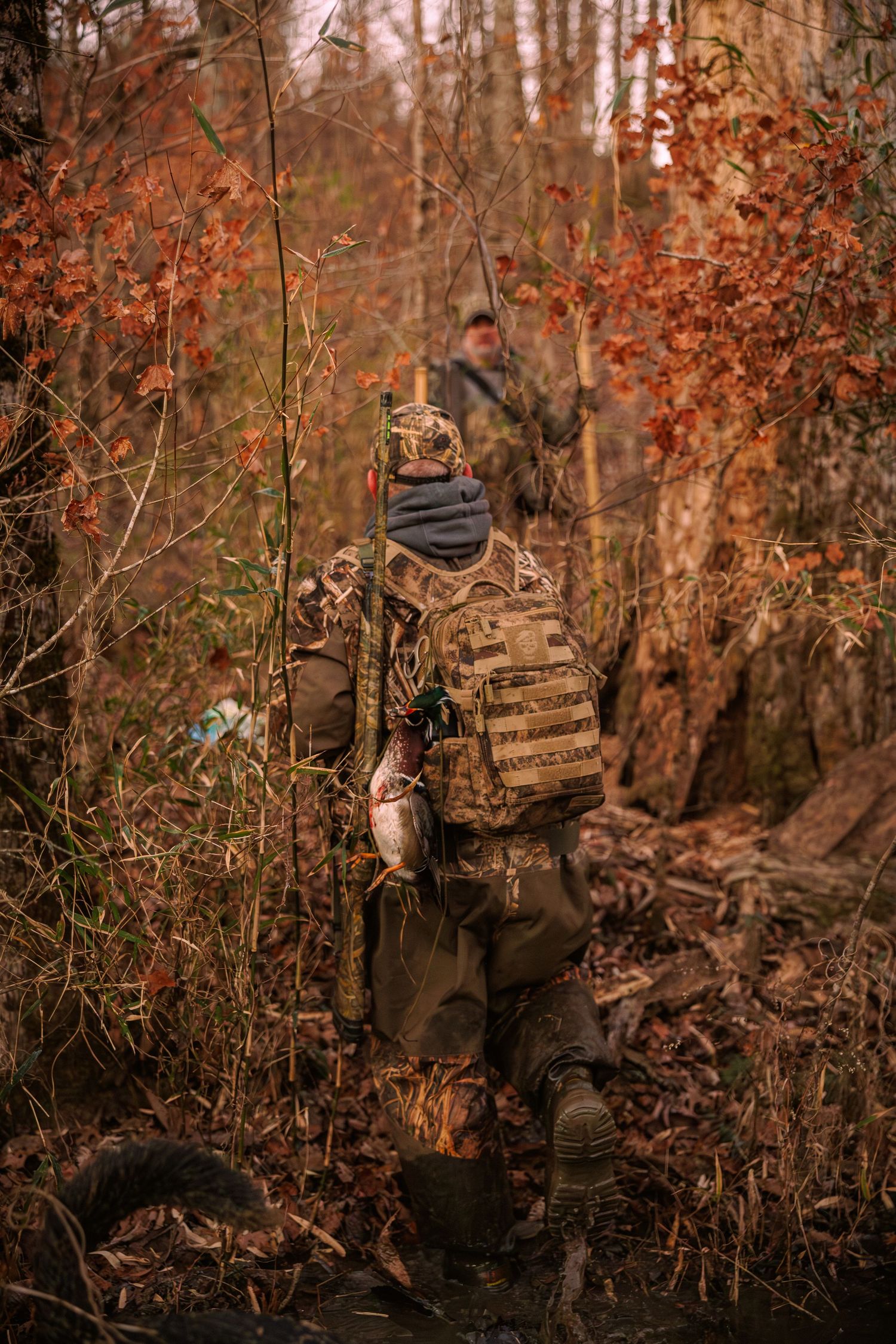 Camouflaged hunter in autumn woods sitting against tree trunk during fall hunting season.