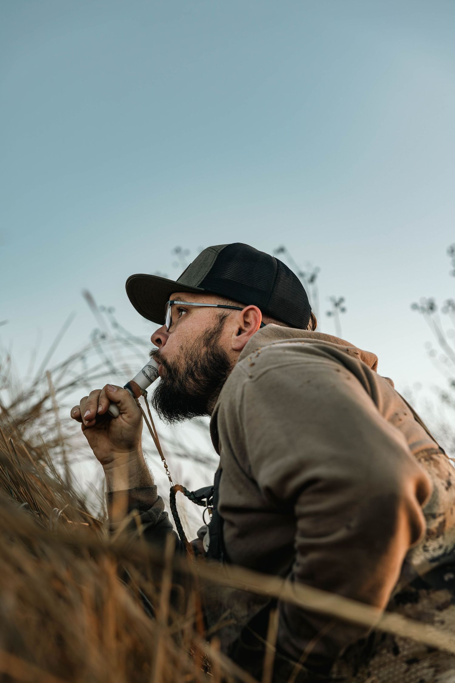 A person wearing a baseball cap looks through binoculars in a field during a nature observation session.