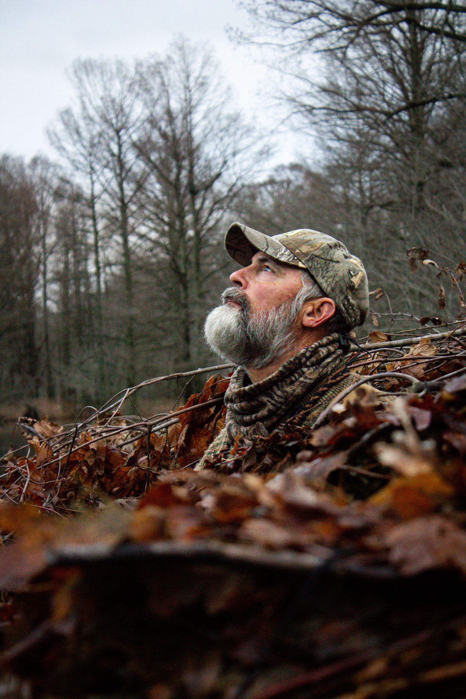 Hunter in camouflage gear lying in fallen autumn leaves during a hunt.