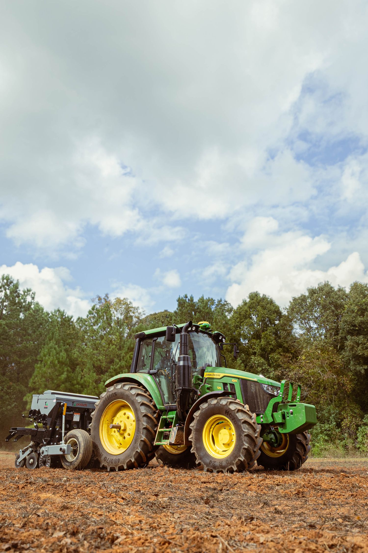 Line of John Deere and green tractors parked in a field under cloudy skies.
