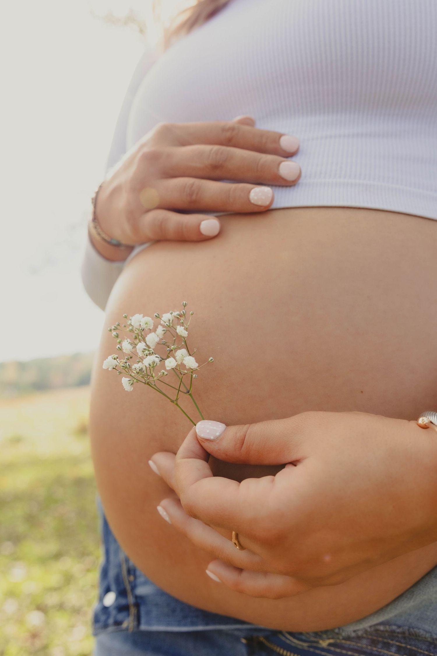 Close-up of pregnant belly with delicate white flowers placed on bare skin.
