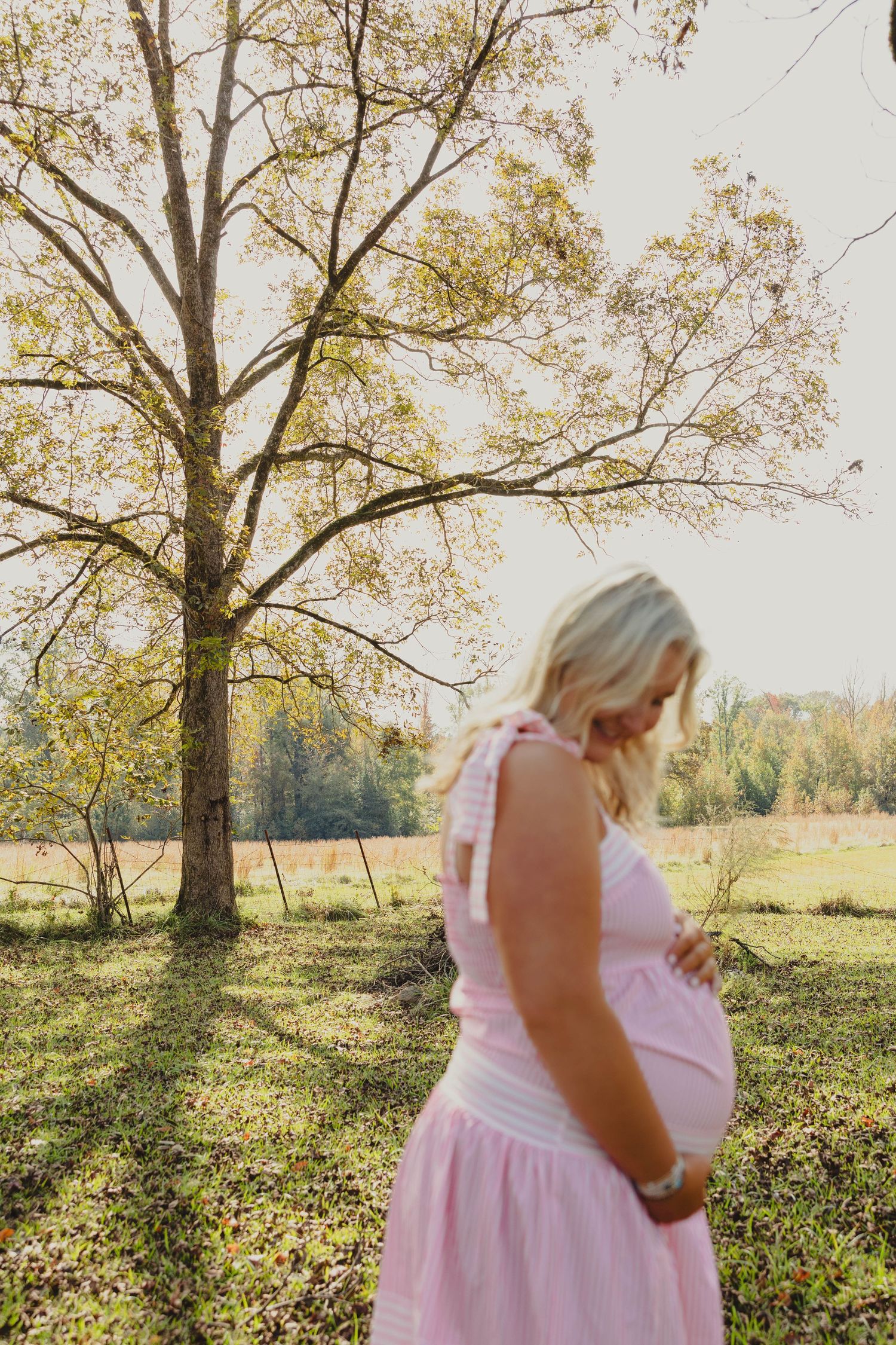 Woman in pink dress walking through autumn field with large trees.