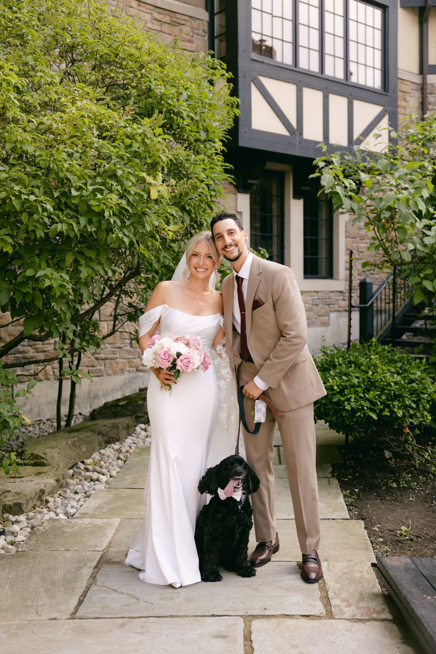 Wedding photos showing a couple posing with their black dog in front of a stone building.