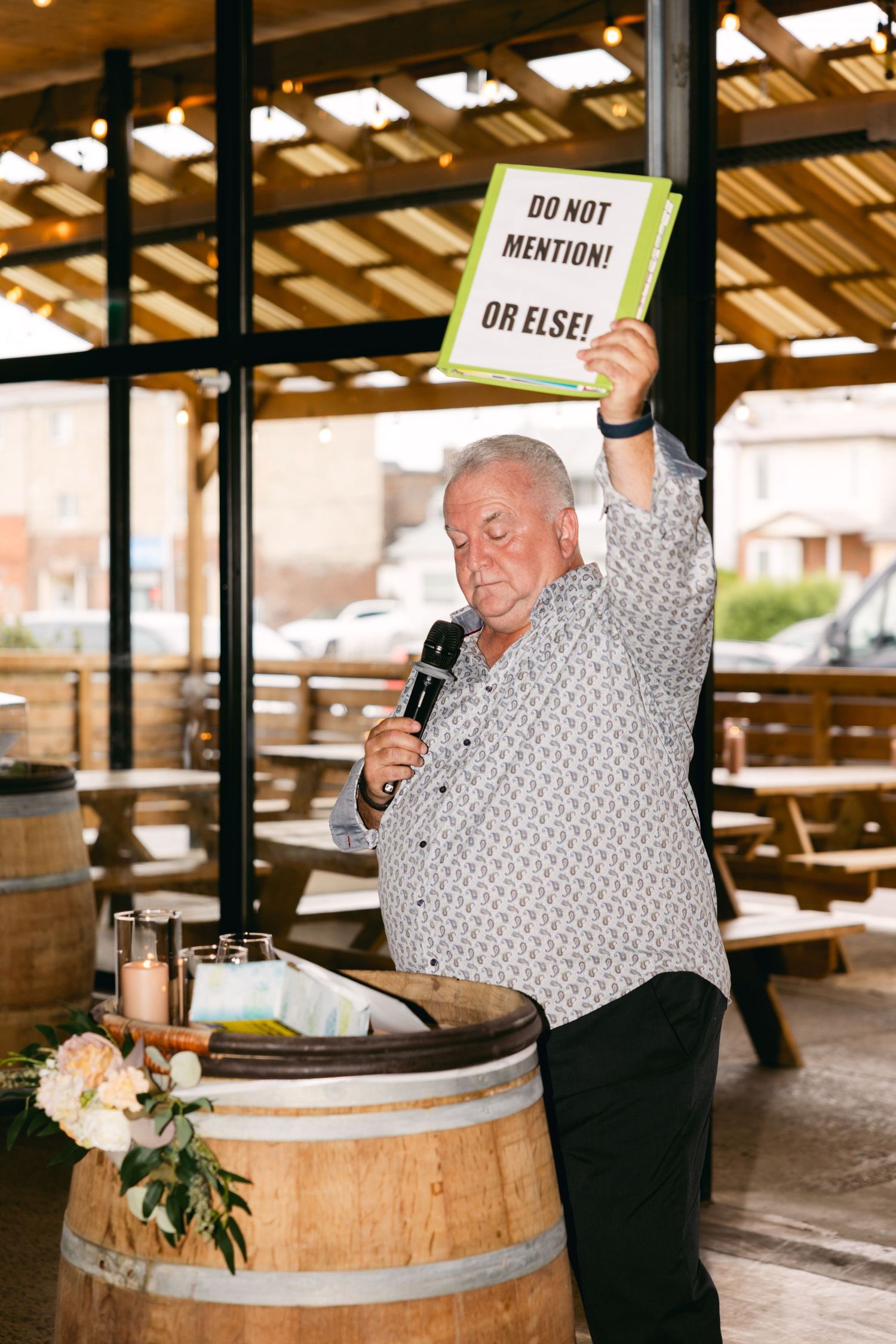 Guest interacts playfully with signs while standing near wooden barrel at wedding reception.