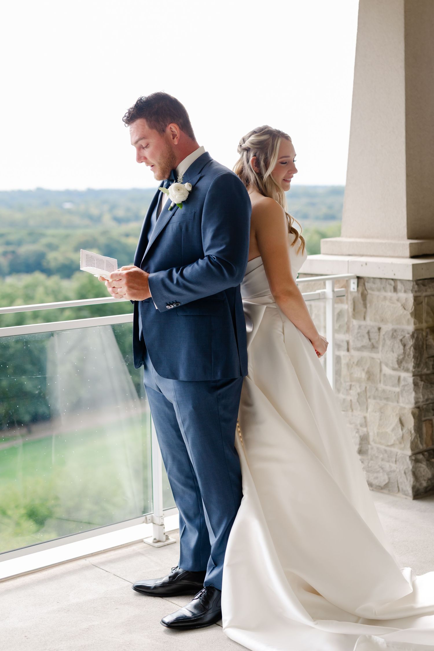 Emotional wedding couple reads letters while standing apart on stone balcony.
