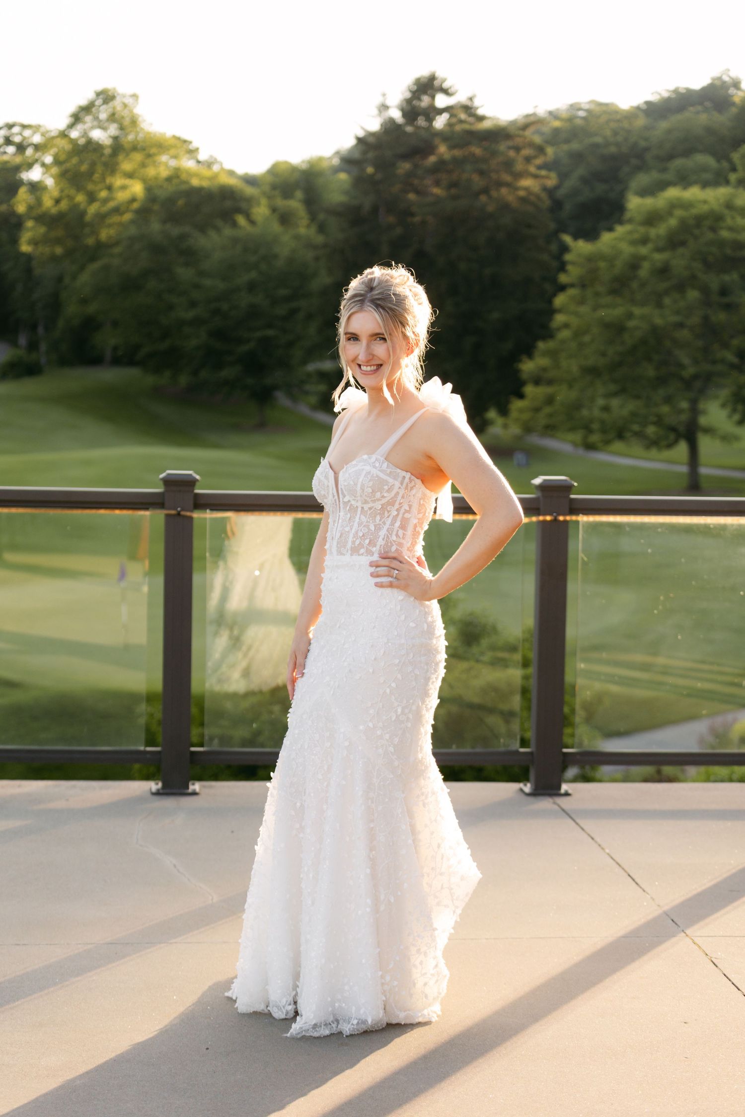 Bride in a detailed lace wedding dress poses on a terrace with scenic golf course views.