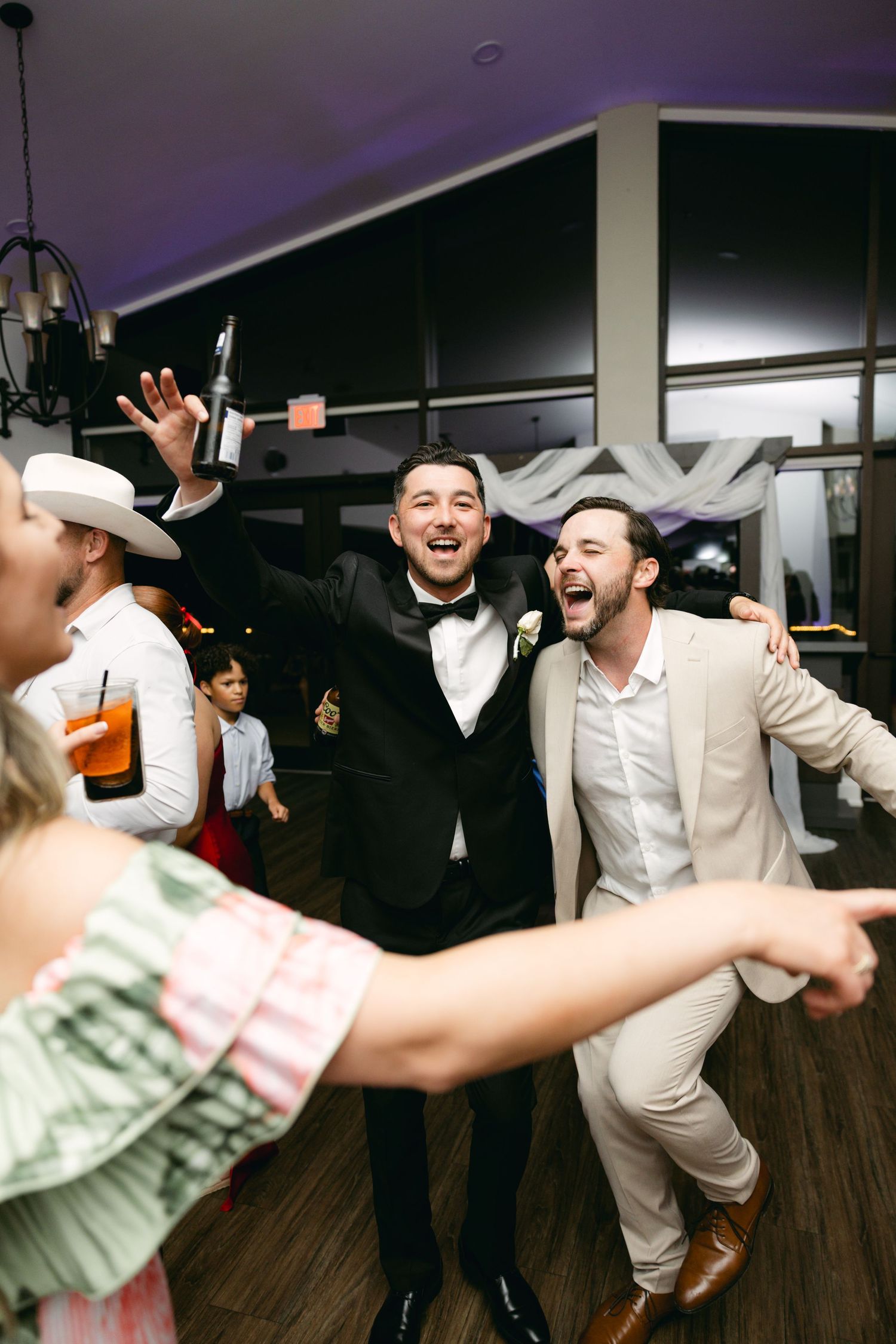 Wedding guests dancing energetically at reception with purple mood lighting.