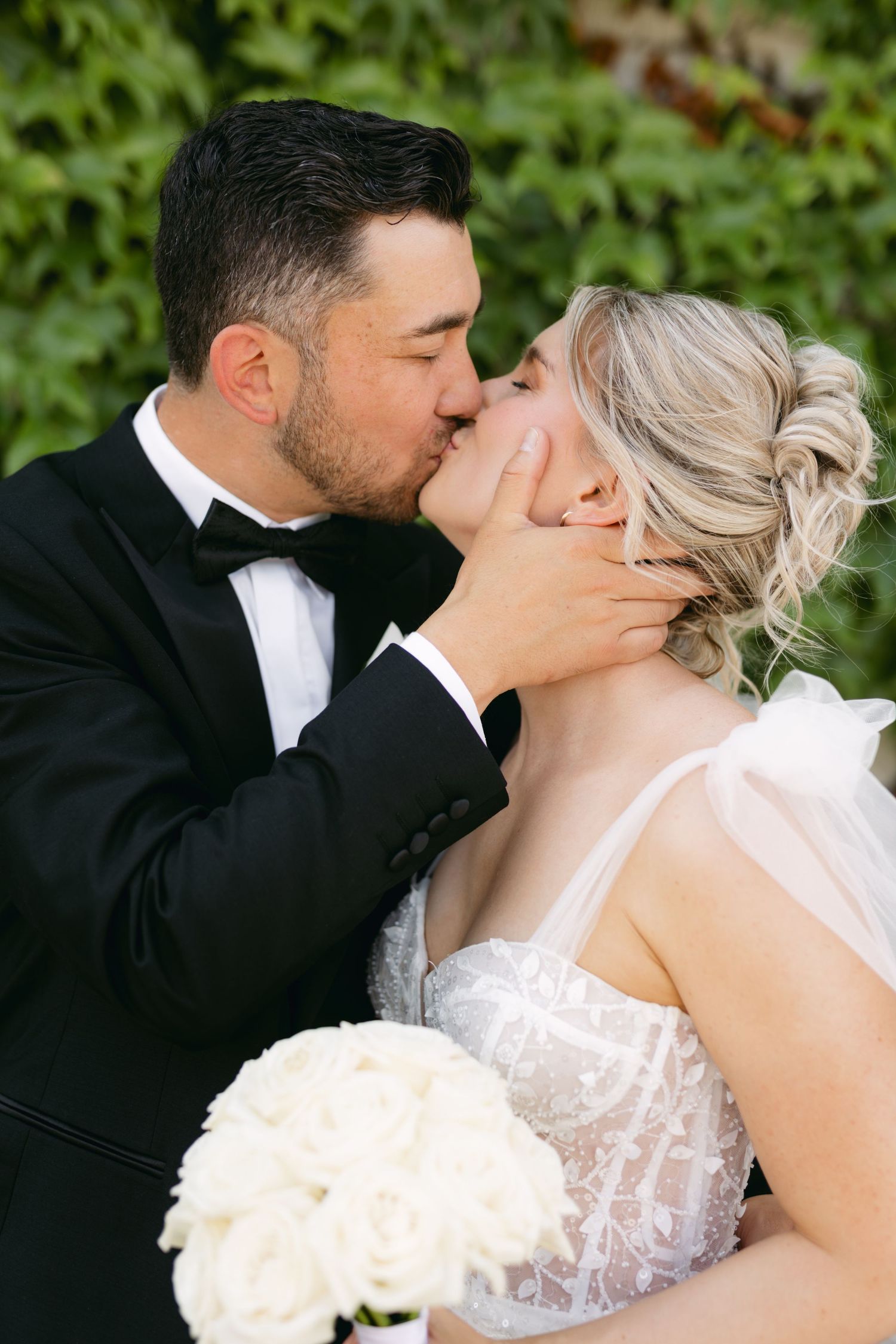 An intimate wedding portrait showing a tender kiss with a white bouquet.