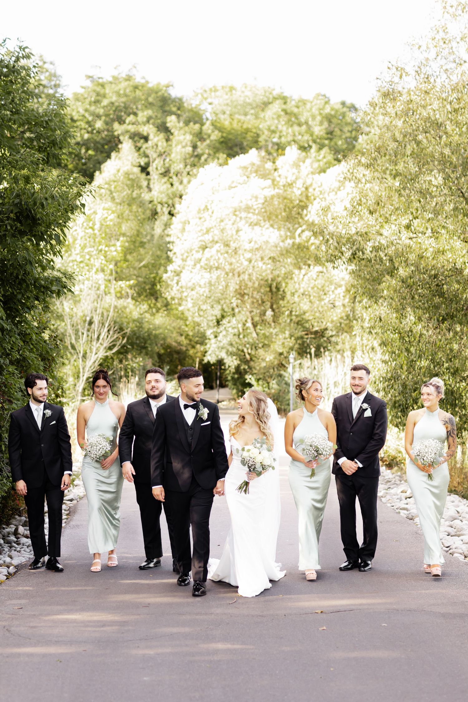 Wedding party in black suits and light dresses walking together on outdoor path.