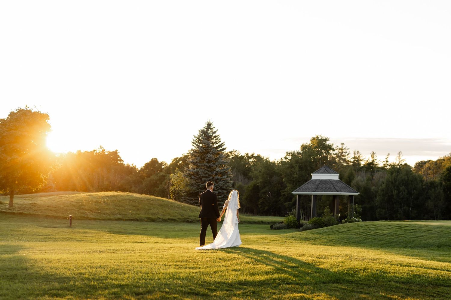 Wedding couple's silhouette against a dramatic sunset on a golf course landscape.