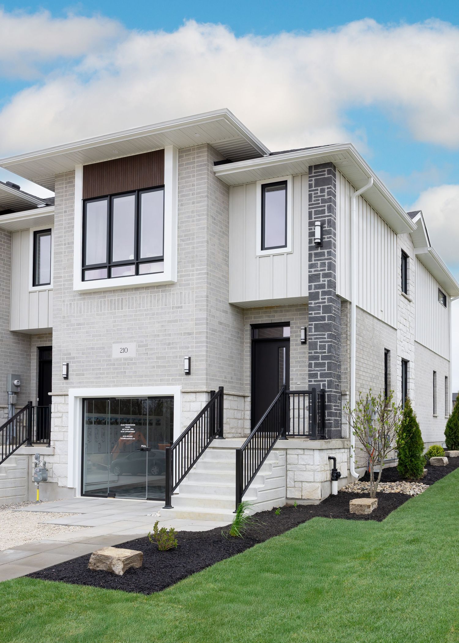 Modern white townhouse exterior with large windows, black railings, and landscaped front yard.