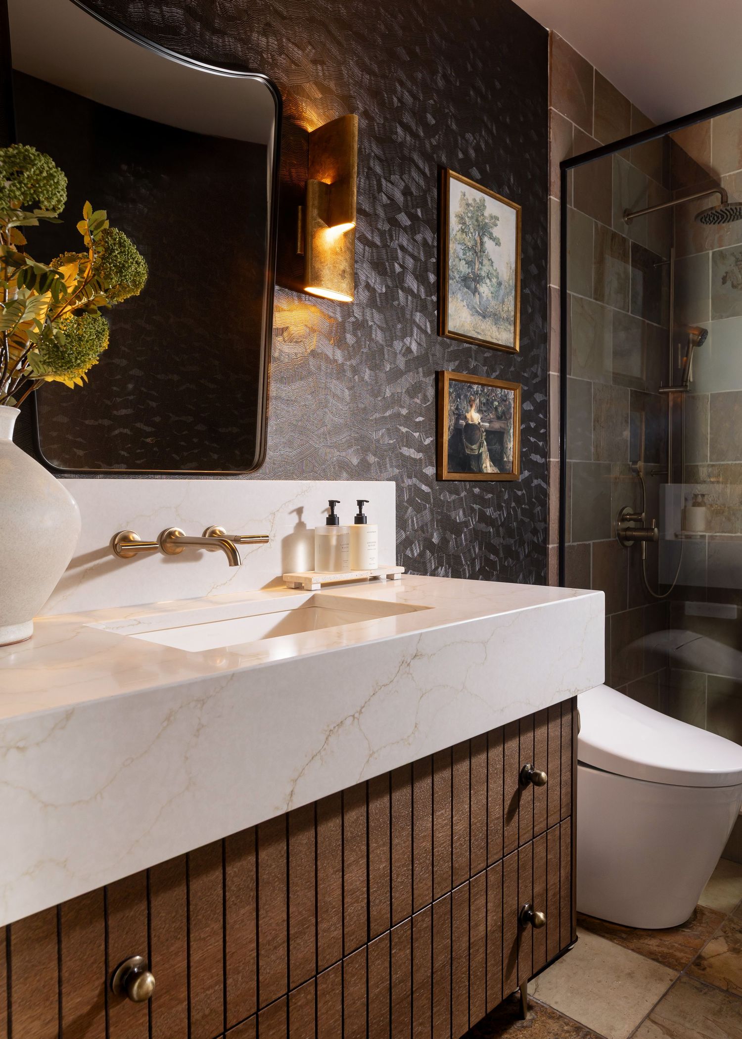 Luxurious bathroom vanity with dark textured wall and white marble countertop illuminated by warm sconces.