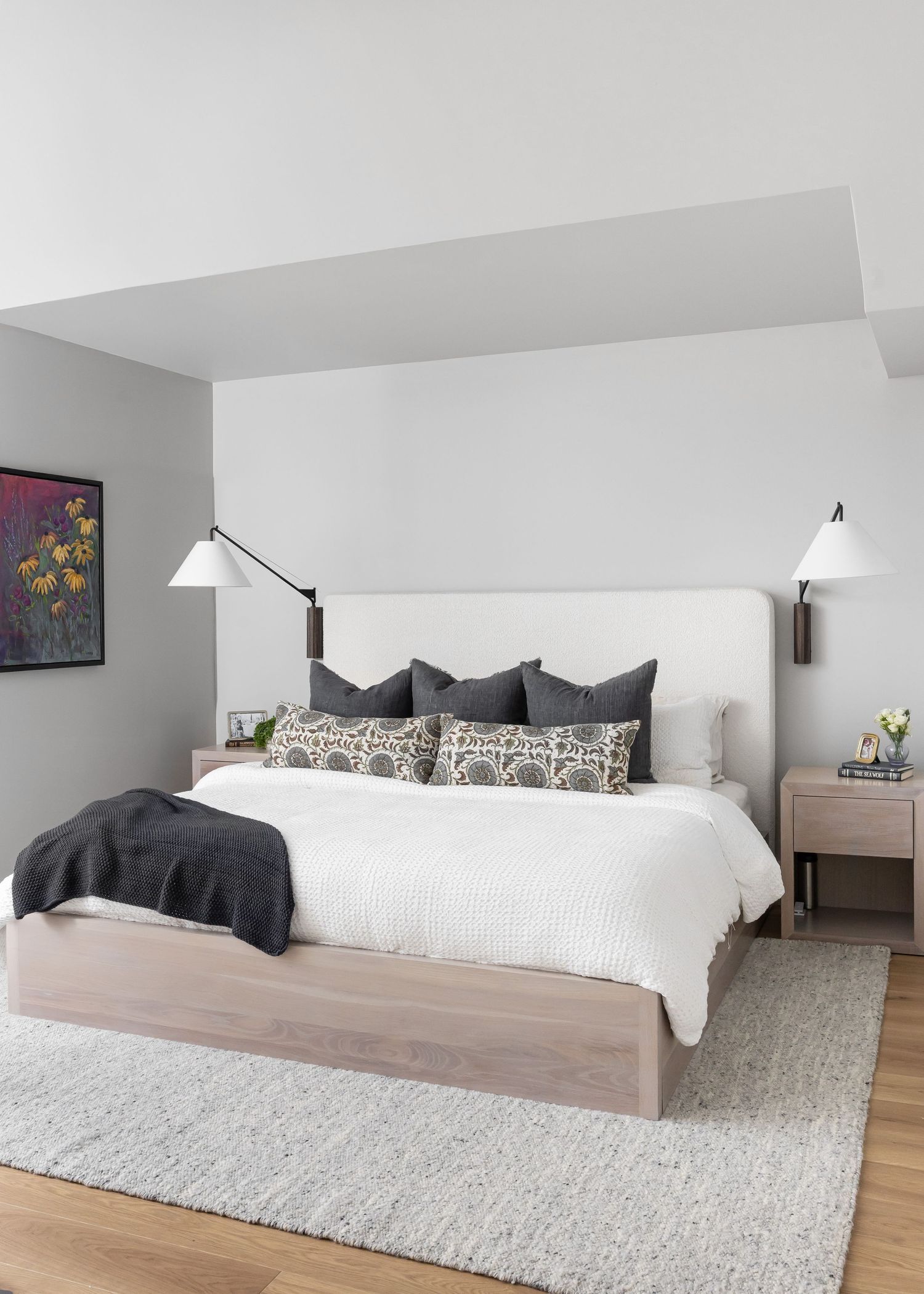 Contemporary bedroom with white bedding, light wood furniture, and plush area rug on hardwood floors.