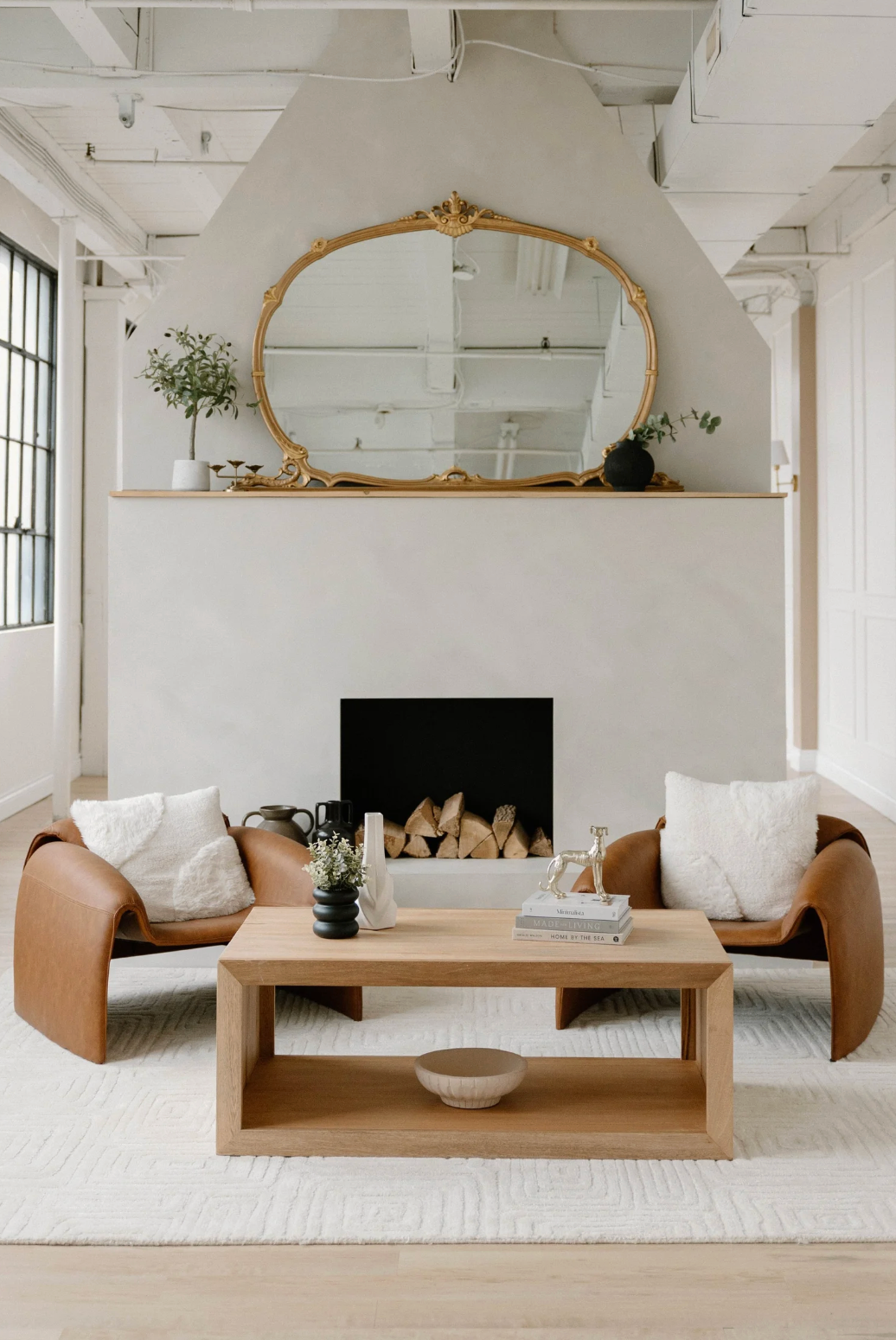 Modern minimalist living room with white walls, wooden coffee table and tan leather sofa in a bright loft space.