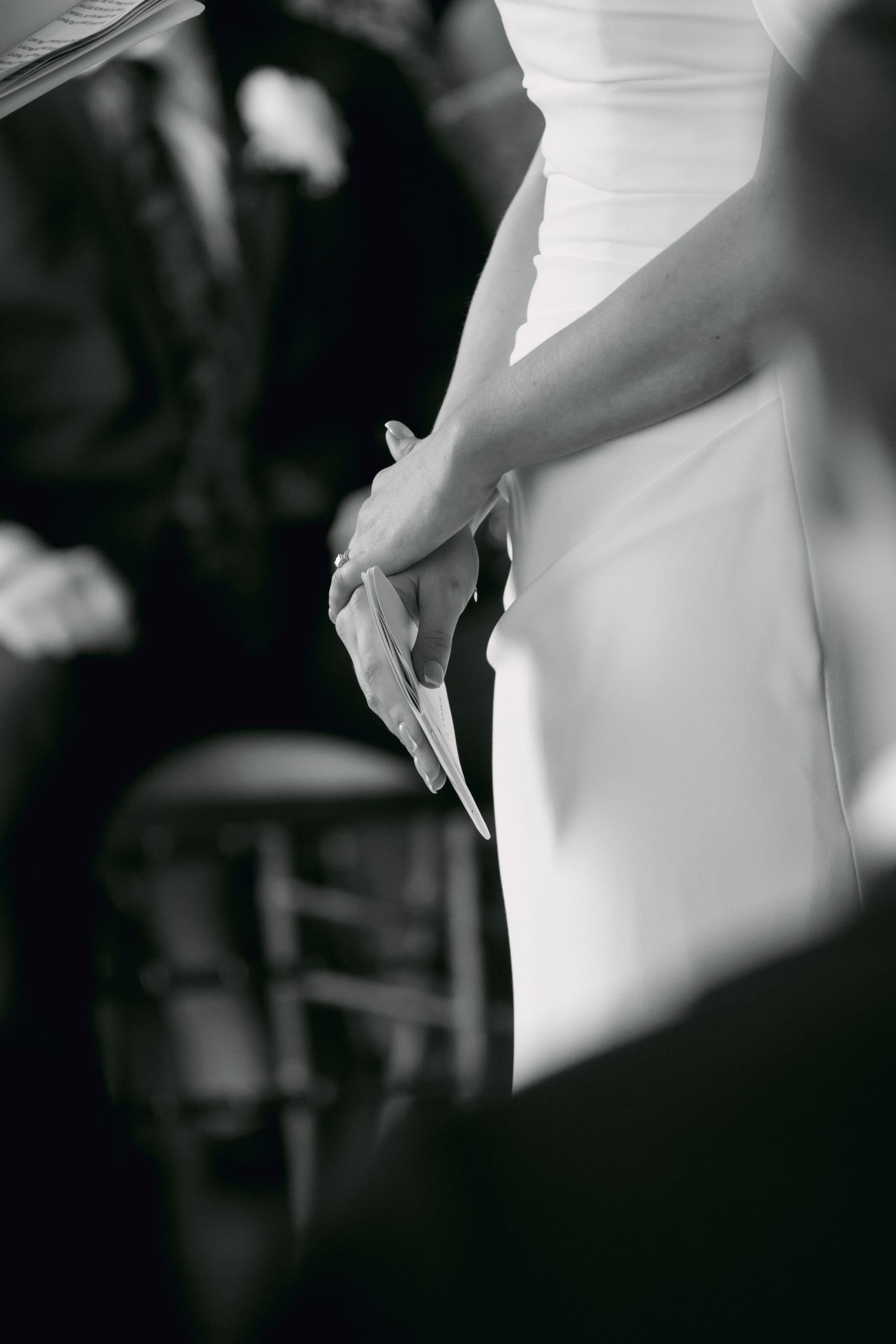 Black and white photo of bride in white dress holding papers during wedding ceremony.