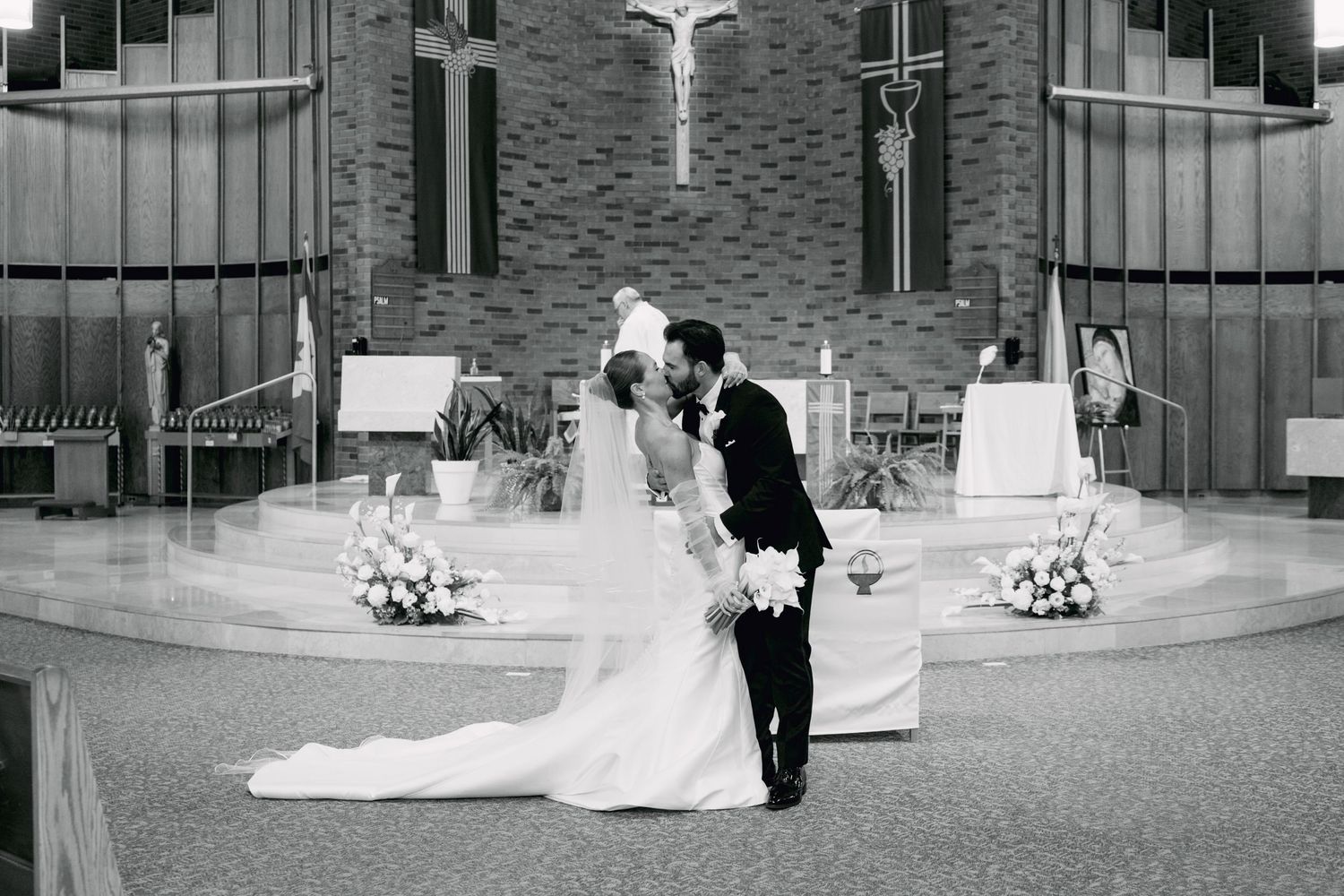 Bride and groom share a kiss at the altar in a black and white wedding photo inside a church.