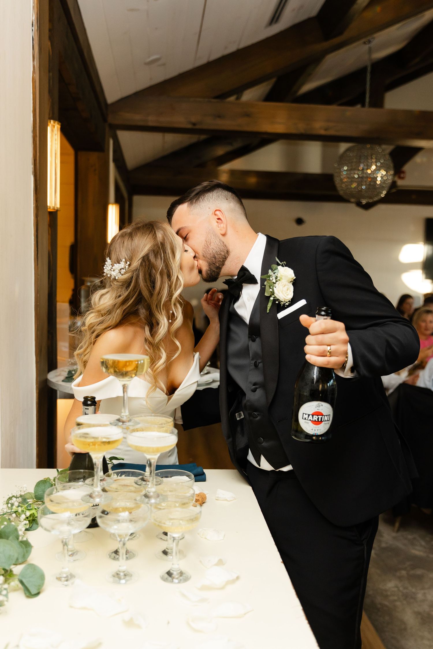 Elegant champagne tower being filled during wedding celebration with decorative greenery.