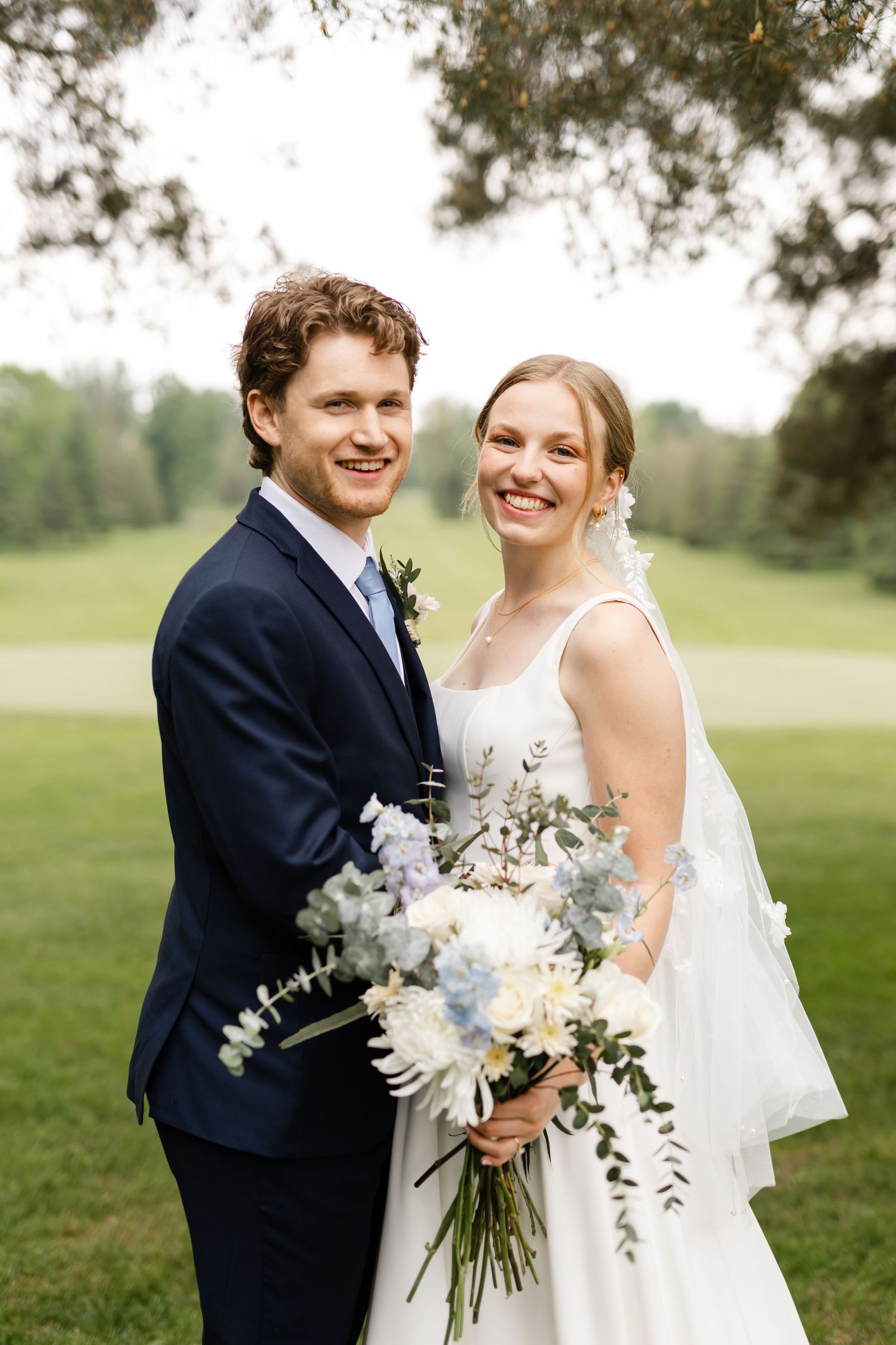 Newlyweds share joyful moment on golf course with white floral bouquet.